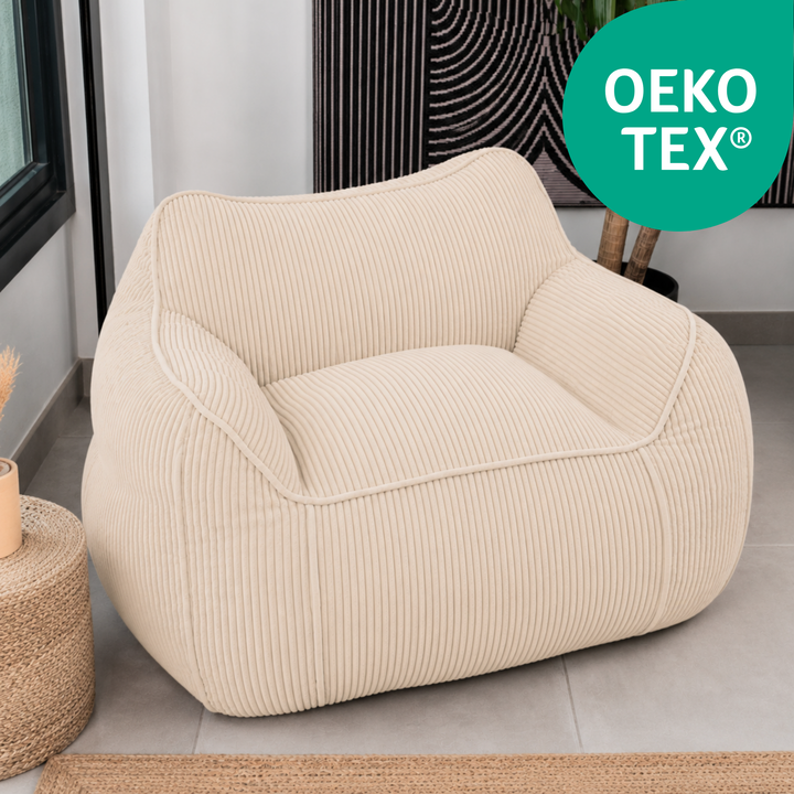 Pouf fauteuil en velours côtelé beige, accoudoirs arrondis et assise profonde, dans un salon