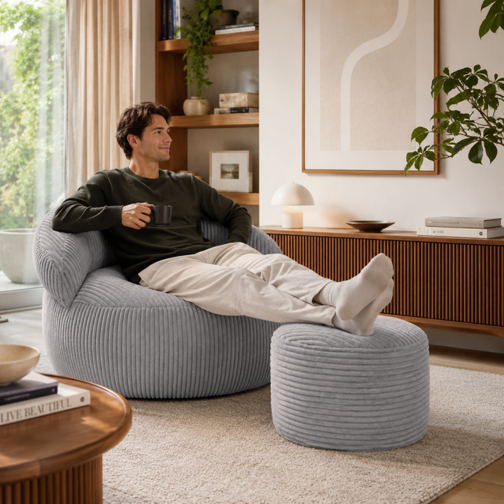 Personne assise confortablement sur un pouf XXL en velours côtelé avec repose-pieds, dans un salon