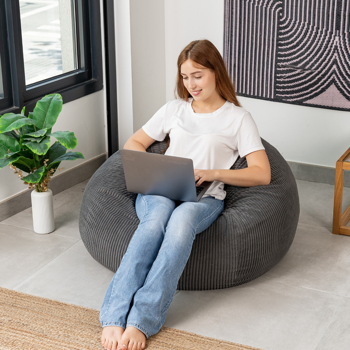 Femme assise sur un pouf poire déhoussable en velours côtelé, dans un salon