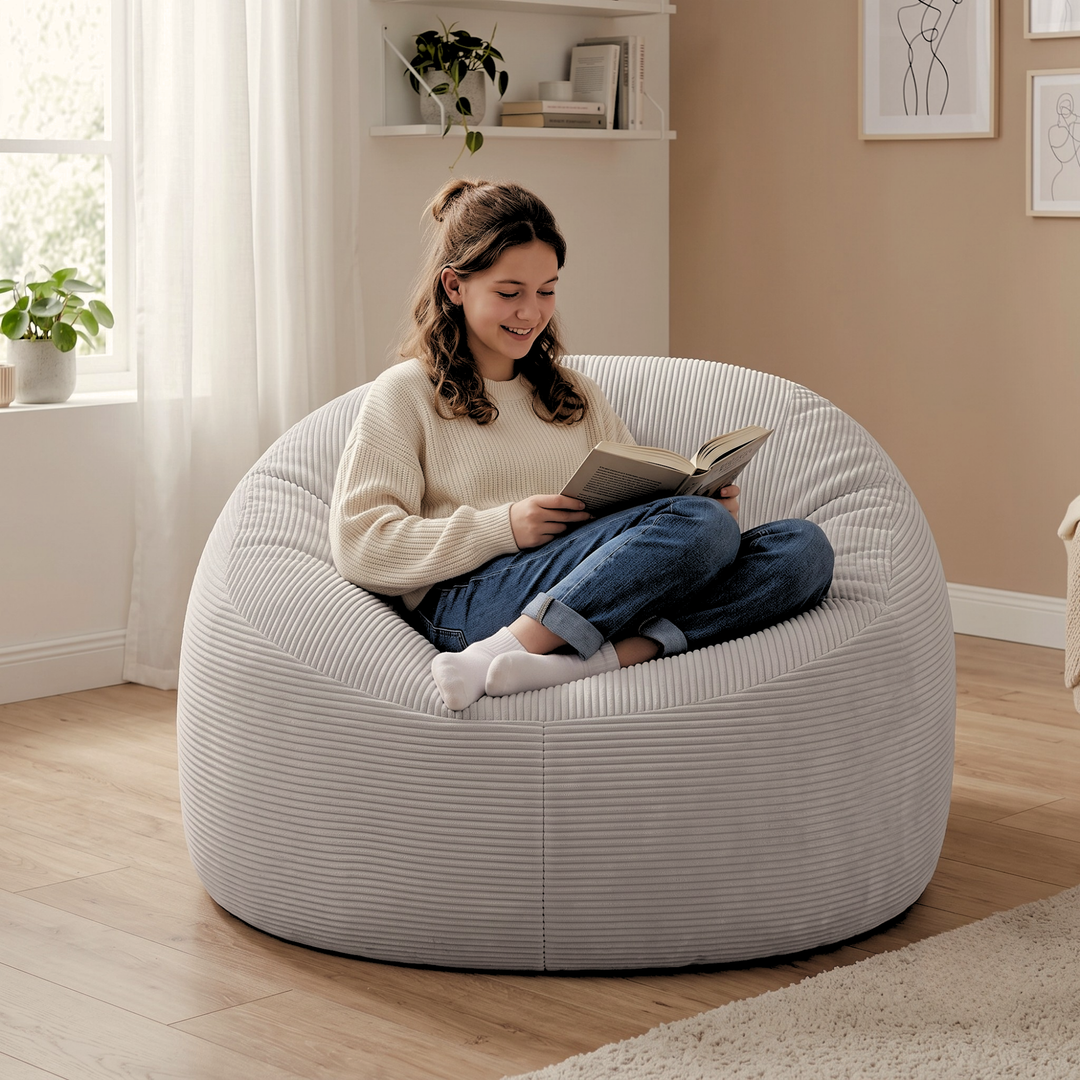 Femme assise sur un pouf déhoussable gris clair en velours côtelé, assise arrondie pour s’asseoir confortablement.