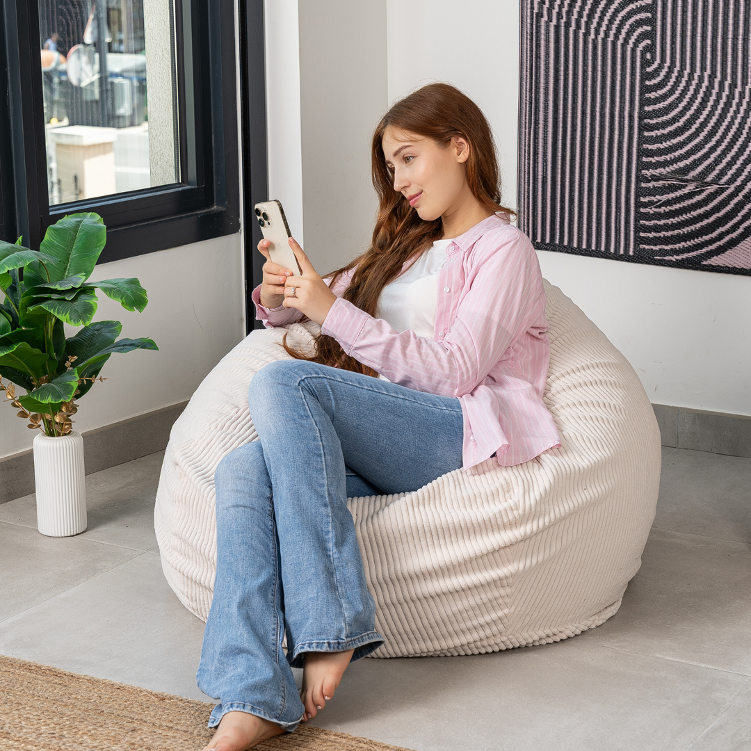 Femme assise sur un pouf poire déhoussable en velours côtelé, dans un salon