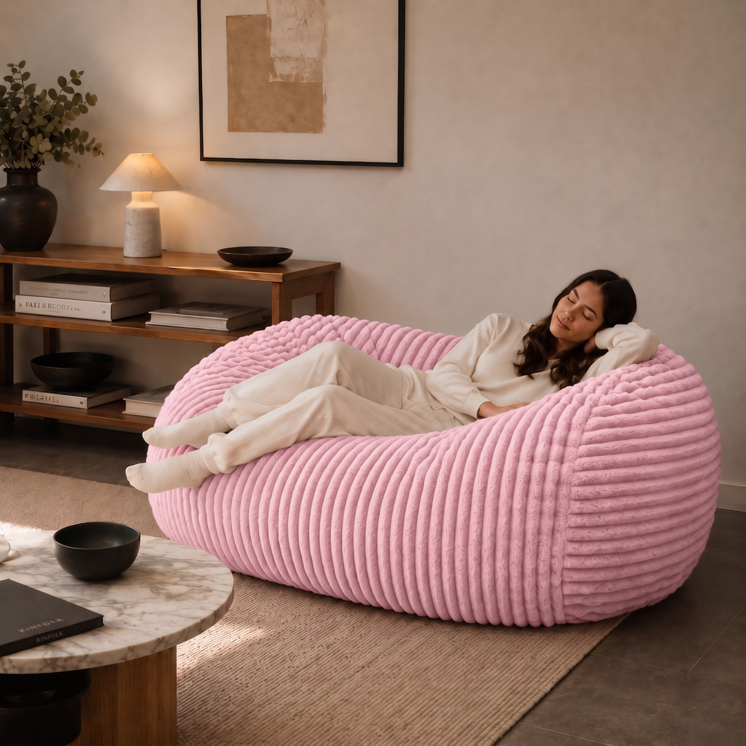 Personne allongée sur un pouf long géant déhoussable rose en fourrure côtelée dans un salon