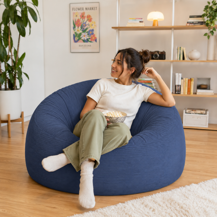 Personne assise sur un pouf déhoussable 100 cm en velours côtelé, dans un salon.